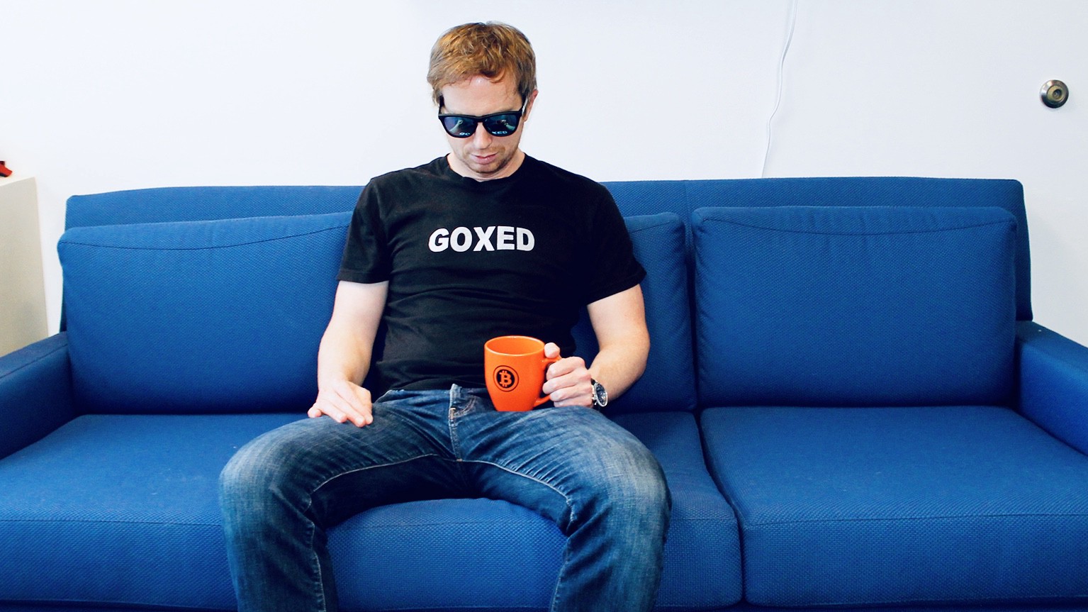 Erik Voorhees, ShapeShift founder sitting on a blue sofa with a t-shirt slogan "GOXED" referring to Mt. Gox crypto hack.